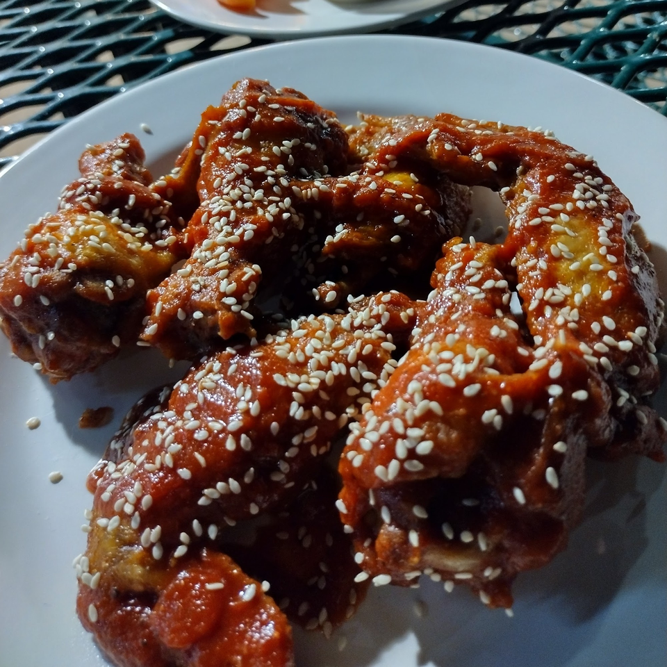 A plate of chicken wings coated in a reddish-brown sauce and sprinkled with sesame seeds.