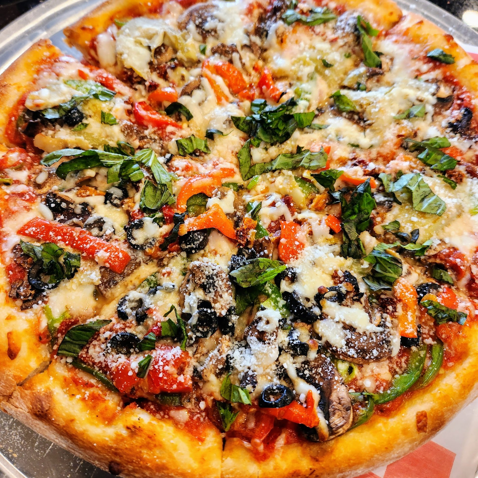 A whole Da Vinci's Pizza Cafe pizza, topped with basil, olives, red peppers, and mushrooms.