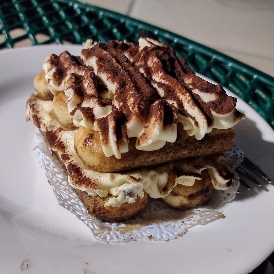 A delicious tiramisu dessert with ladyfingers, cream, and cocoa powder on a white plate.